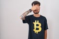 Young hispanic man with tattoos wearing bitcoin t shirt covering eyes with hand, looking serious and sad Royalty Free Stock Photo