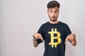 Young hispanic man with tattoos wearing bitcoin t shirt pointing down with fingers showing advertisement, surprised face and open