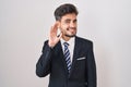 Young hispanic man with tattoos wearing business suit and tie smiling with hand over ear listening an hearing to rumor or gossip Royalty Free Stock Photo