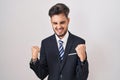 Young hispanic man with tattoos wearing business suit and tie very happy and excited doing winner gesture with arms raised, Royalty Free Stock Photo