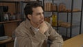 Young hispanic man thinking in an office setting with shelves in the background indicating a workplace environment, showcasing Royalty Free Stock Photo