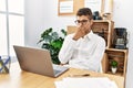 Young hispanic man thinking working with laptop at business office