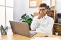 Young hispanic man thinking working with laptop at business office