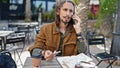 Young hispanic man tourist talking on smartphone holding credit card sitting on table at coffee shop terrace Royalty Free Stock Photo