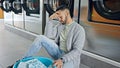 Young hispanic man upset sitting on the floor at laundry facility