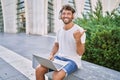 Young hispanic man using headphones and laptop at street pointing thumb up to the side smiling happy with open mouth Royalty Free Stock Photo