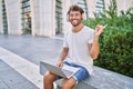 Young hispanic man using headphones and laptop at street smiling happy pointing with hand and finger to the side Royalty Free Stock Photo