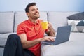Young hispanic man using laptop and drinking coffee sitting on floor at home Royalty Free Stock Photo