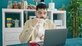 Young hispanic man using laptop having breakfast at dinning room Royalty Free Stock Photo