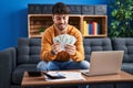 Young hispanic man using laptop holding dollars sitting on sofa at home Royalty Free Stock Photo