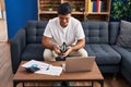Young hispanic man using laptop holding wallet with dollars at home Royalty Free Stock Photo