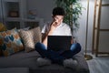 Young hispanic man using laptop at home at night pointing to the eye watching you gesture, suspicious expression Royalty Free Stock Photo