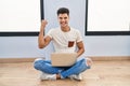 Young hispanic man using laptop at home very happy and excited doing winner gesture with arms raised, smiling and screaming for Royalty Free Stock Photo