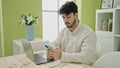 Young hispanic man using laptop and smartphone sitting on table at dinning room Royalty Free Stock Photo