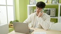 Young hispanic man using laptop talking on smartphone at dinning room Royalty Free Stock Photo