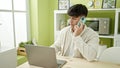 Young hispanic man using laptop talking on smartphone at dinning room Royalty Free Stock Photo