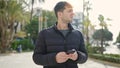 Young hispanic man using smartphone looking away at park Royalty Free Stock Photo