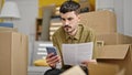 Young hispanic man using smartphone reading document at new home Royalty Free Stock Photo