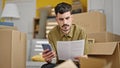 Young hispanic man using smartphone reading document at new home Royalty Free Stock Photo