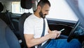 Young hispanic man using smartphone sitting on car at street Royalty Free Stock Photo