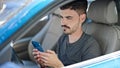 Young hispanic man using smartphone sitting on car at street Royalty Free Stock Photo