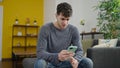 Young hispanic man using smartphone worried sitting on the sofa at home Royalty Free Stock Photo