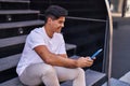 Young hispanic man using touchpad sitting on stairs at street Royalty Free Stock Photo