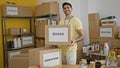 Young hispanic man volunteer holding books package to donate smiling at charity center Royalty Free Stock Photo