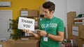 Young hispanic man volunteer pointing to thank you banner smiling at charity center Royalty Free Stock Photo