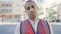 Young hispanic man volunteer wearing vest looking serious at street