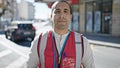 Young hispanic man volunteer wearing vest looking serious at street