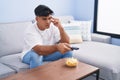 Young hispanic man watching movie with boring expression at home Royalty Free Stock Photo