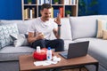 Young hispanic man watching video on laptop on how to use first aid kit doing ok sign with fingers, smiling friendly gesturing