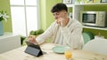 Young hispanic man watching video on touchpad having breakfast at dinning room Royalty Free Stock Photo