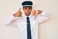 Young hispanic man wearing airplane pilot uniform doing thumbs up and down, disagreement and agreement expression