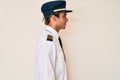 Young hispanic man wearing airplane pilot uniform looking to side, relax profile pose with natural face and confident smile