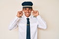 Young hispanic man wearing airplane pilot uniform smiling pulling ears with fingers, funny gesture Royalty Free Stock Photo