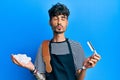 Young hispanic man wearing barber apron holding razor and foam looking at the camera blowing a kiss being lovely and sexy