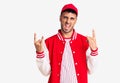 Young hispanic man wearing baseball uniform shouting with crazy expression doing rock symbol with hands up