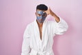 Young hispanic man wearing beauty face mask and bath robe pointing unhappy to pimple on forehead, ugly infection of blackhead Royalty Free Stock Photo