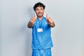 Young hispanic man wearing blue male nurse uniform approving doing positive gesture with hand, thumbs up smiling and happy for Royalty Free Stock Photo