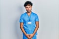 Young hispanic man wearing blue male nurse uniform skeptic and nervous, frowning upset because of problem