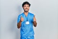 Young hispanic man wearing blue male nurse uniform success sign doing positive gesture with hand, thumbs up smiling and happy Royalty Free Stock Photo