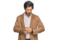 Young hispanic man wearing business clothes checking the time on wrist watch, relaxed and confident Royalty Free Stock Photo