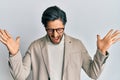 Young hispanic man wearing business jacket and glasses celebrating mad and crazy for success with arms raised and closed eyes Royalty Free Stock Photo