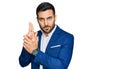 Young hispanic man wearing business jacket holding symbolic gun with hand gesture, playing killing shooting weapons, angry face