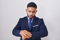 Young hispanic man wearing business suit and tie checking the time on wrist watch, relaxed and confident Royalty Free Stock Photo