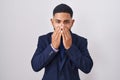 Young hispanic man wearing business suit and tie laughing and embarrassed giggle covering mouth with hands, gossip and scandal Royalty Free Stock Photo