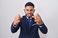 Young hispanic man wearing business suit and tie shouting frustrated with rage, hands trying to strangle, yelling mad Royalty Free Stock Photo