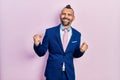 Young hispanic man wearing business suit and tie very happy and excited doing winner gesture with arms raised, smiling and Royalty Free Stock Photo